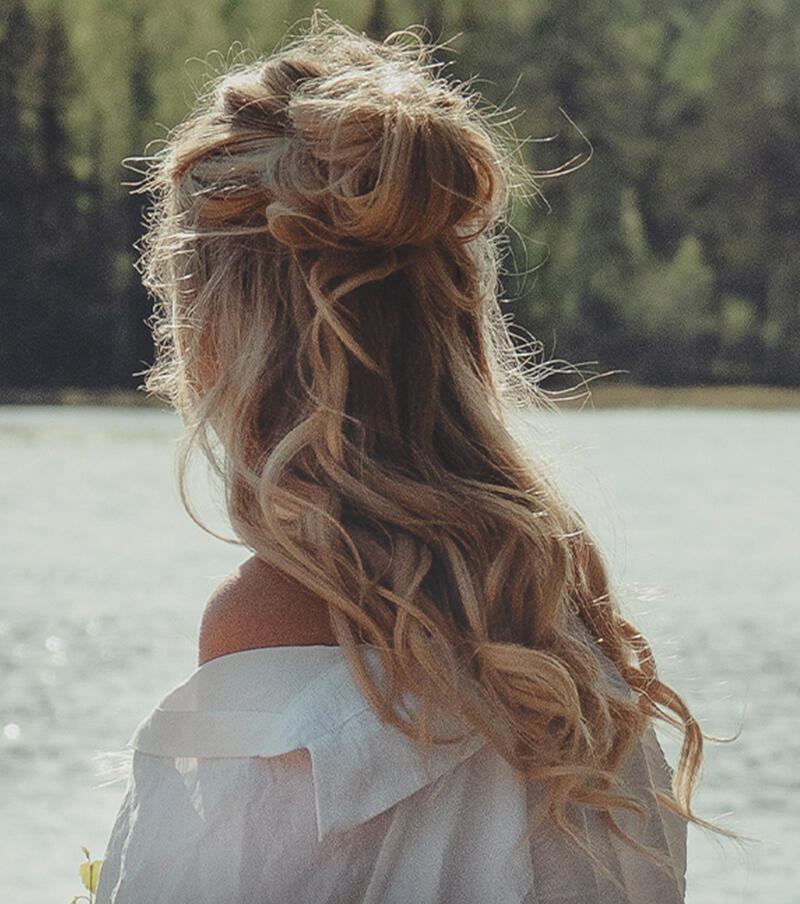 Kvinna bakifrån med Cendre Ash Blonde Mix extensions i en håruppsättning framför havet